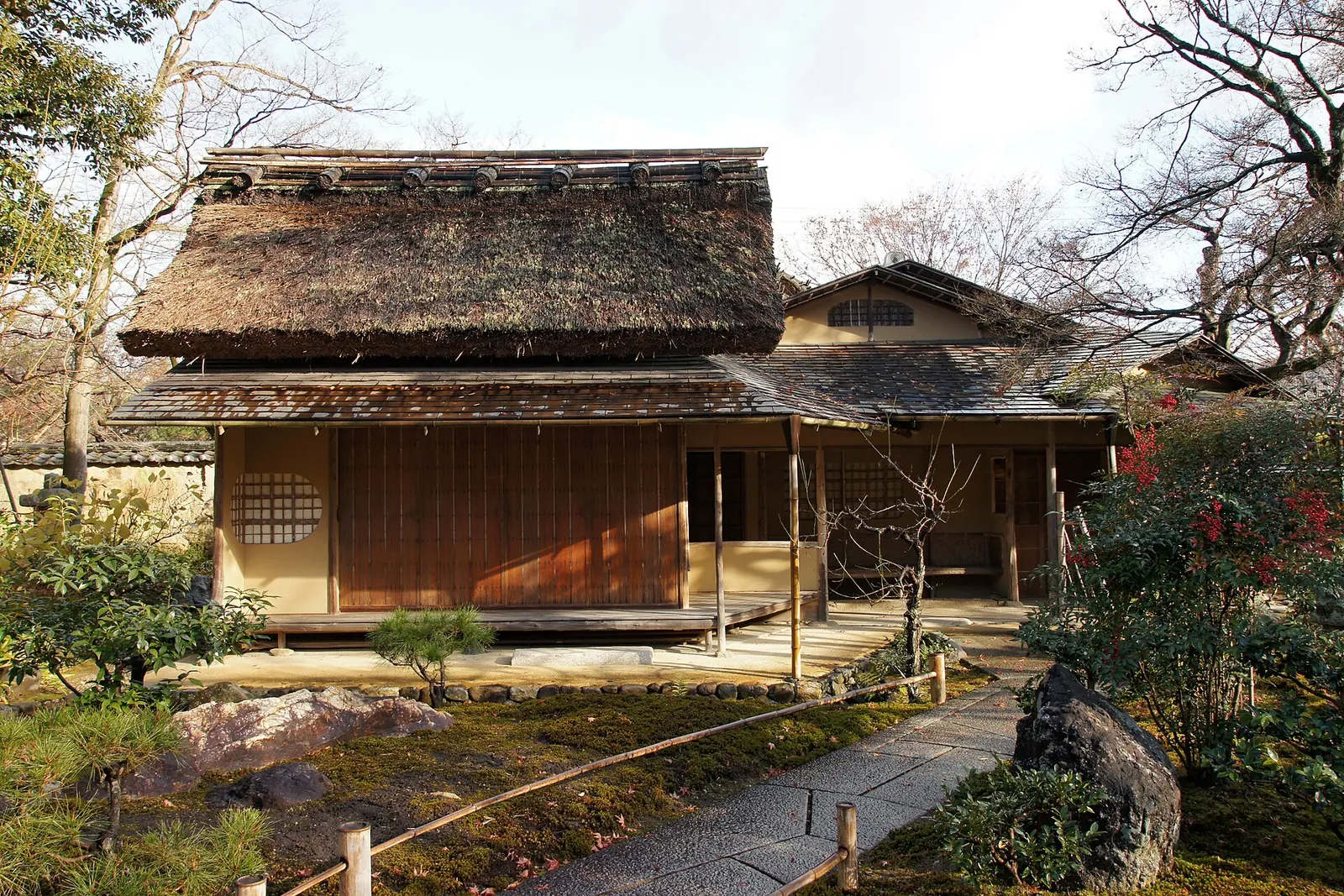 A thatched teahouse with a wooden veranda in the garden of Hōgon-in, a Kyoto temple, with maples, a stone path and rocks